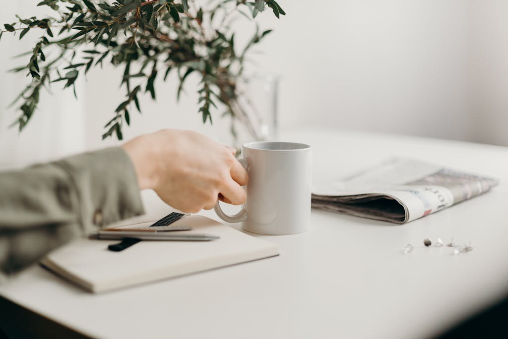 A minimalist workspace featuring a mug, notebook, and greenery, perfect for productivity.